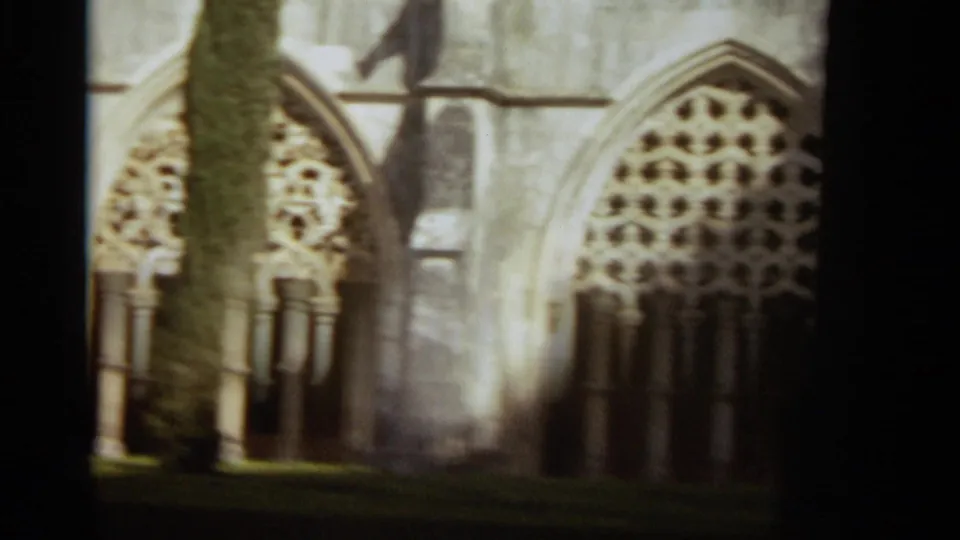 1965 8mm frame from Nazaré showing a tree trunk in front of Gothic-style church windows and weathered stonework.