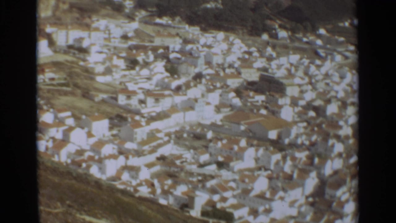 Aerial view over dense white houses and terracotta roofs in a coastal town.