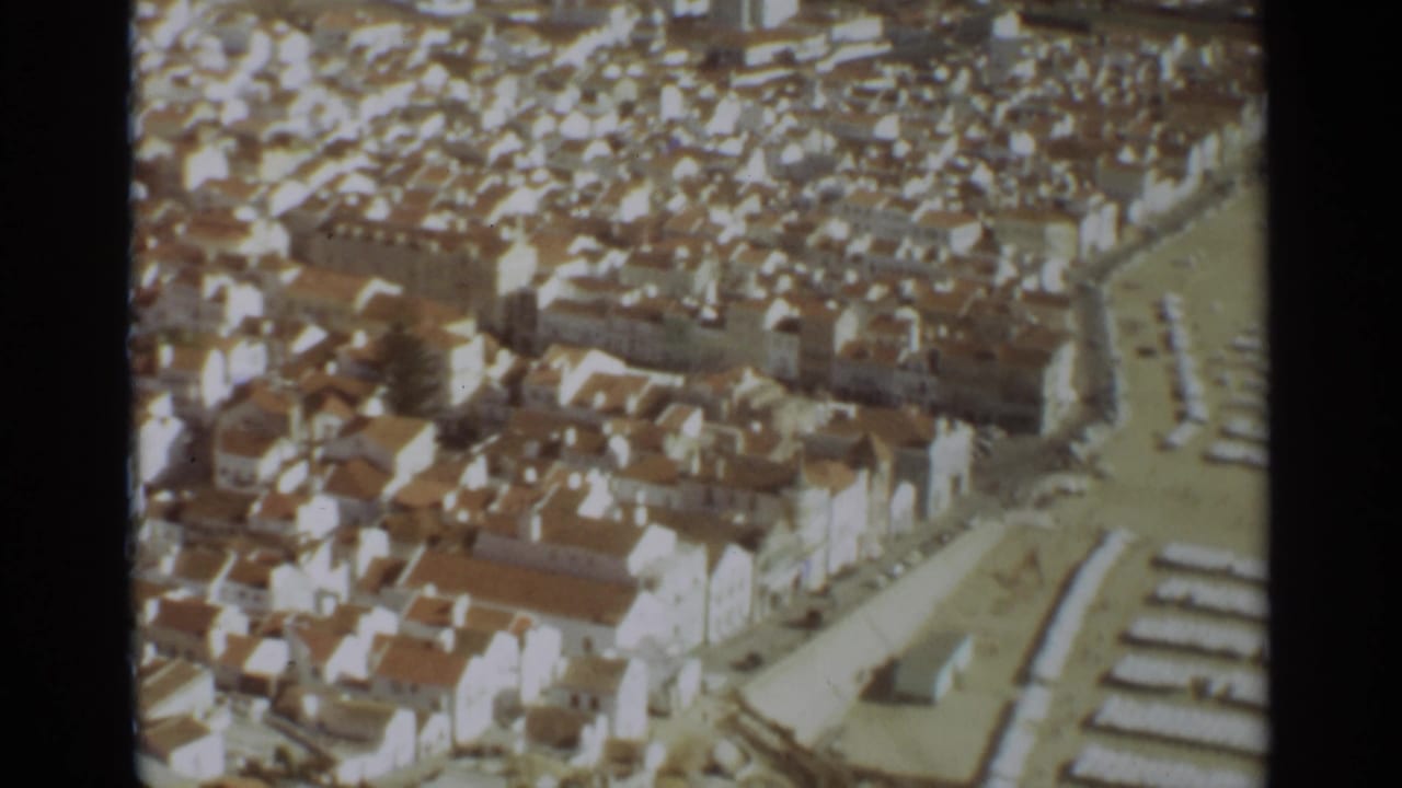 1965 8mm aerial view over Nazare, Portugal, showing white buildings with terracotta roofs near the beach.