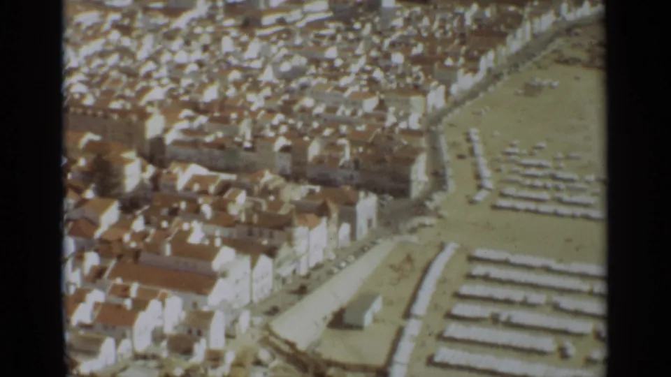 Nazare, Portugal, seen from above in 1965 with clustered houses, beach rows, and pale sand near the shore.