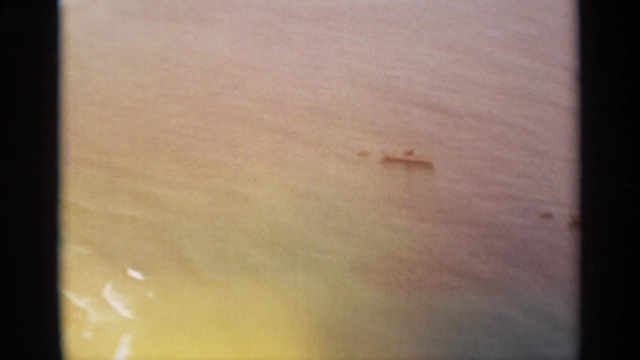1965 Nazare, Portugal coastal view with open water and small distant boats near shore, tinted by warm 8mm color fade.