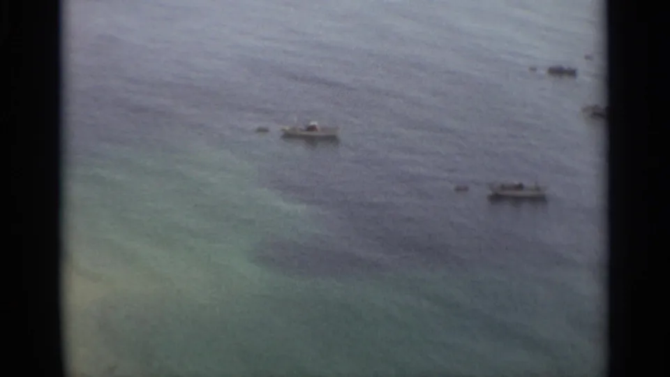 1965 Nazare, Portugal home-movie frame showing multiple small boats scattered across calm coastal water.