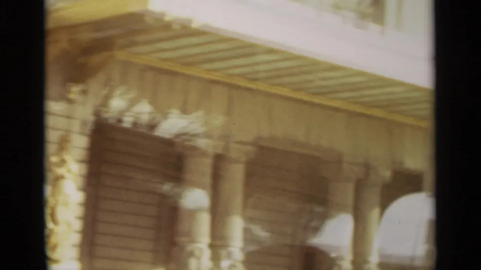 1965 Nazare, Portugal frame showing a blurred seaside building detail with a slatted roof, columns, and shaded wall.
