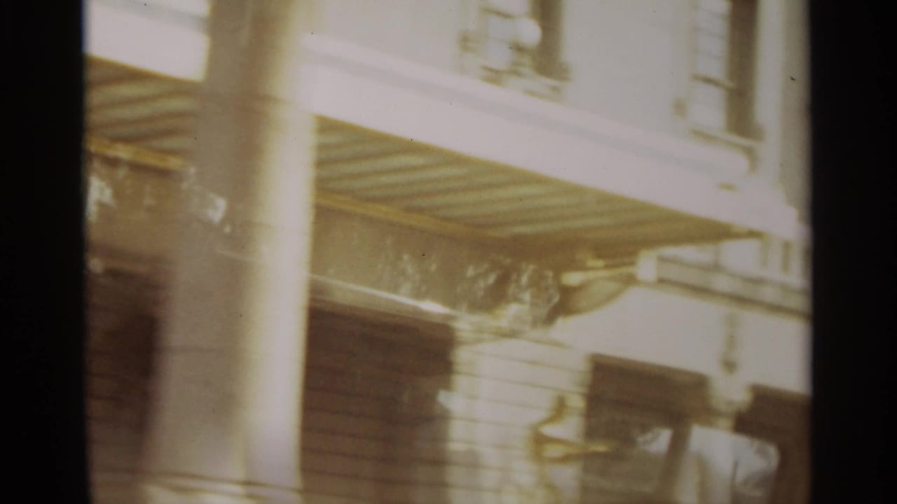 Sunlit building facade with columns, shuttered windows, and a balcony edge.