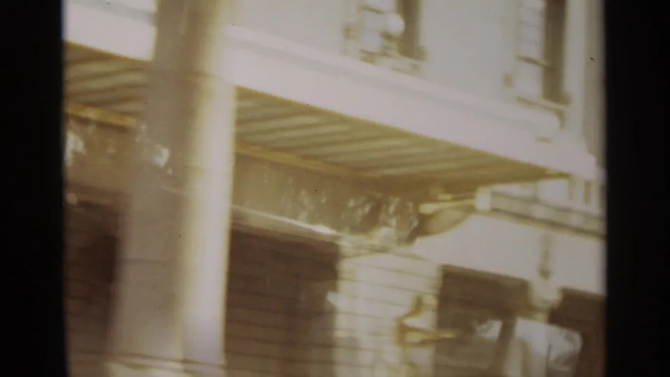 1965 Nazare home-movie frame showing a bright exterior facade with shutters, balcony railings, columns, and strong overexposure.
