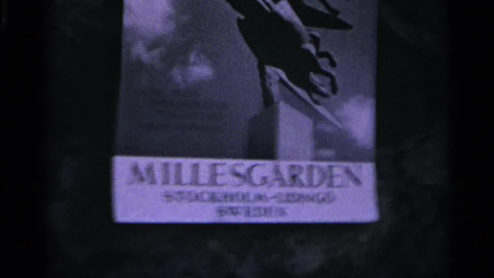1965 Nazare frame showing a dark, bluish sign or poster area with “MILLESGARDEN” text and a cropped sculptural figure above.