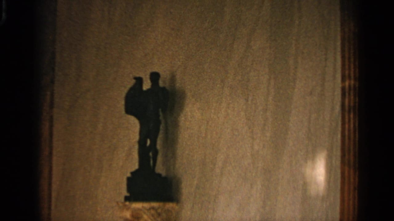 Dark standing figurine silhouetted on a pedestal against a tan interior wall.