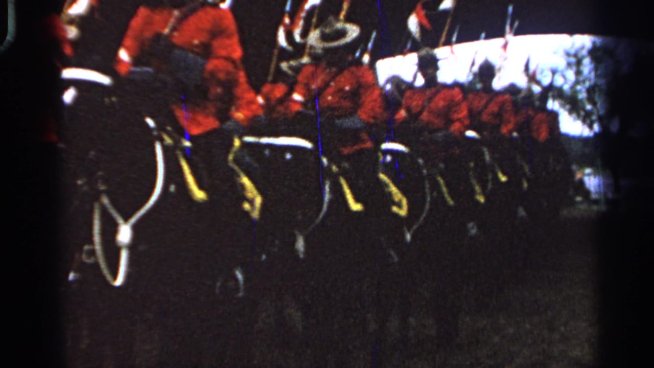 Mounted officers in red jackets ride in formation past the camera with flags raised behind them.