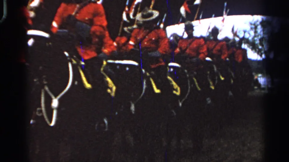 In 1965 Saint Louis home-movie footage, mounted uniformed riders in red serge-style jackets pass close to the camera in a formal line.