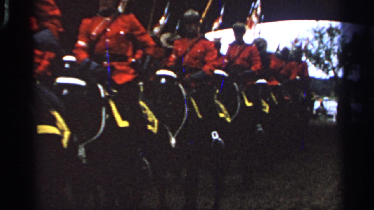 A line of red-uniformed mounted riders continues across a grassy area with flags visible overhead.