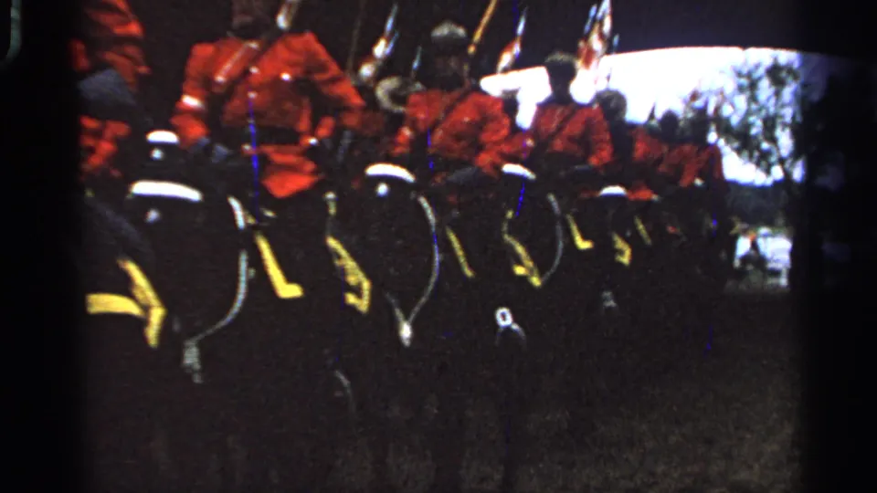 Mounted ceremonial riders in red jackets and dark hats ride in a line, with flags and horse tack visible in the 8mm frame.