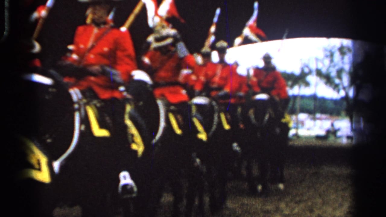 Mounted uniformed riders in red jackets approach the camera in parade formation.