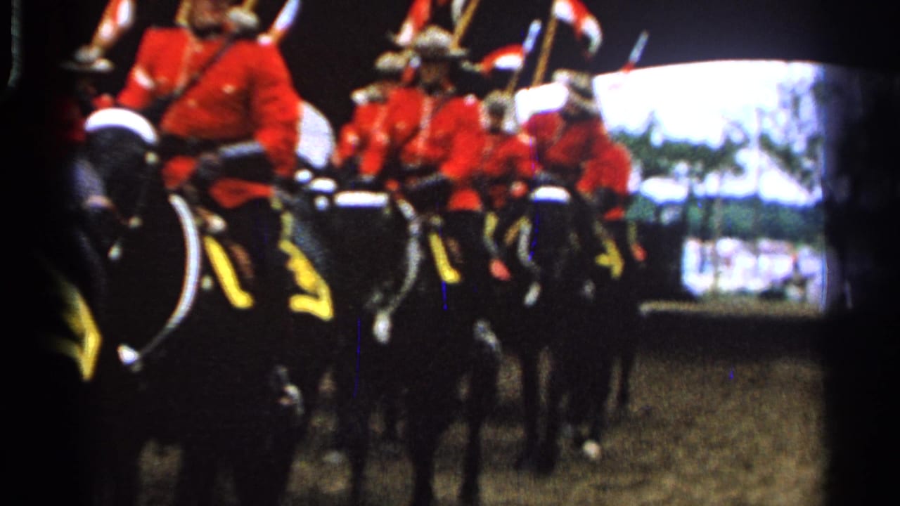 Riders in red uniforms on dark horses pass in close formation outdoors.