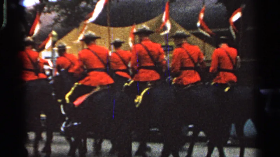 Red-jacketed mounted riders proceed away from the camera under flags in the 1965 Saint Louis parade scene.