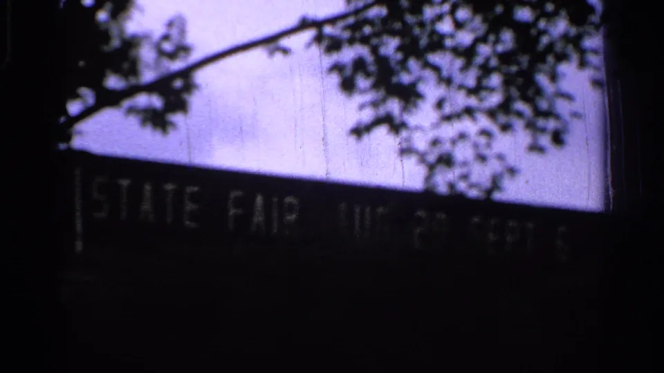 The final frame holds on the STATE FAIR sign, partly obscured by darkness and tree branches in the grainy 8mm scan.