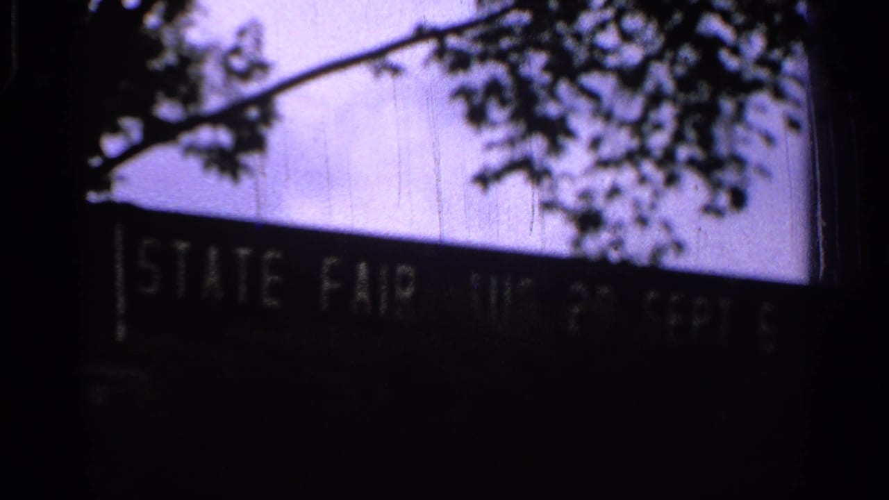 1965 Missouri 8mm frame showing a silhouetted state fair date sign beneath tree branches at dusk or night.