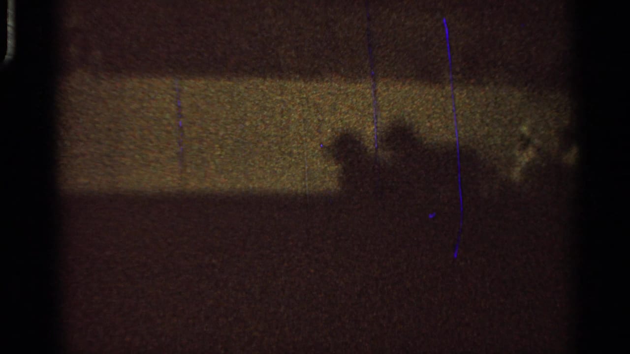 Grainy low-light fairground view with distant human or rider silhouettes crossing a dark outdoor area.
