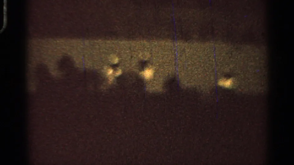 Low-light 8mm view of a nighttime fair event, with small bright lights and indistinct figures near the horizon.