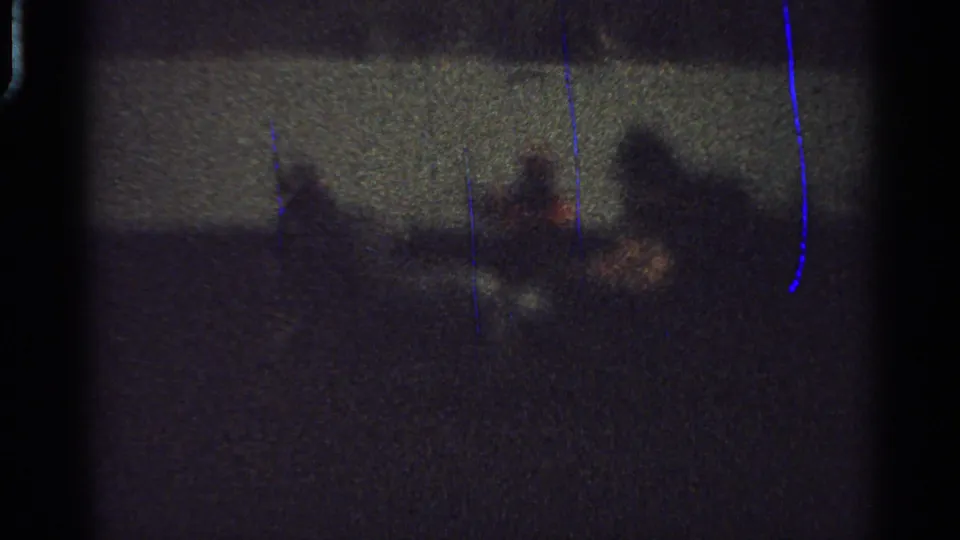 Low-light 1965 Saint Louis frame with shadowy figures and a probable carriage or horse shape crossing an indoor event floor behind a barrier.