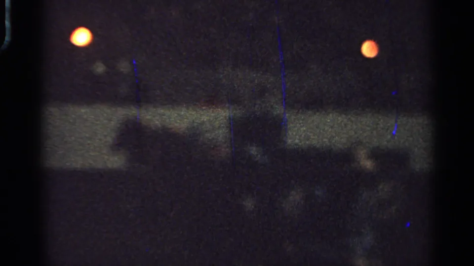 Soft 1965 Saint Louis home-movie frame of a dark indoor event area with rail barrier, warm lights, and blurred spectator silhouettes.