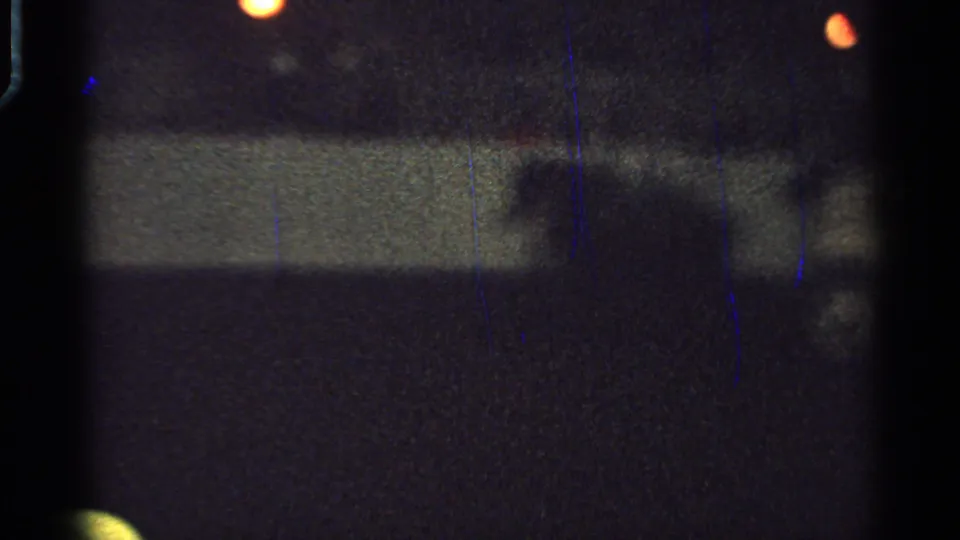 Low-light 1965 Saint Louis 8mm frame showing orange lights over a pale barrier-like band with little detail visible beneath.