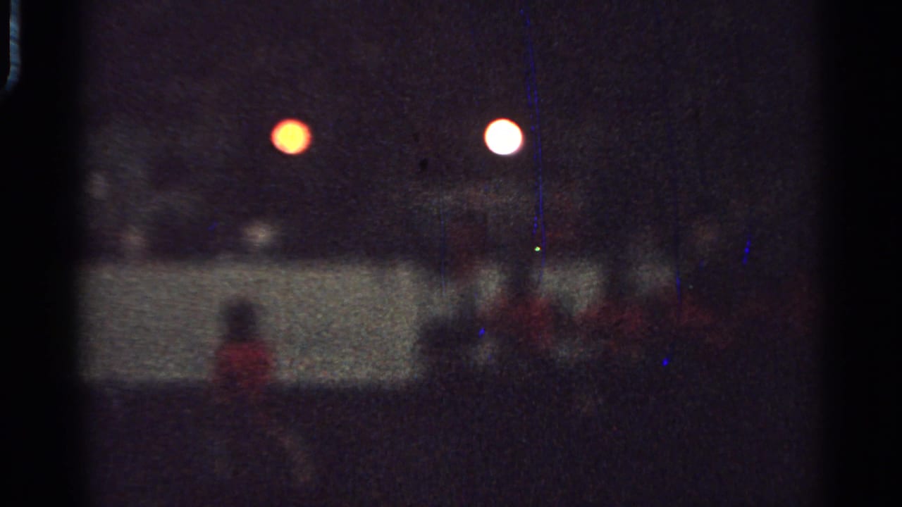 Grainy 1965 Saint Louis 8mm frame showing a red-coated rider on horseback in a nighttime procession.