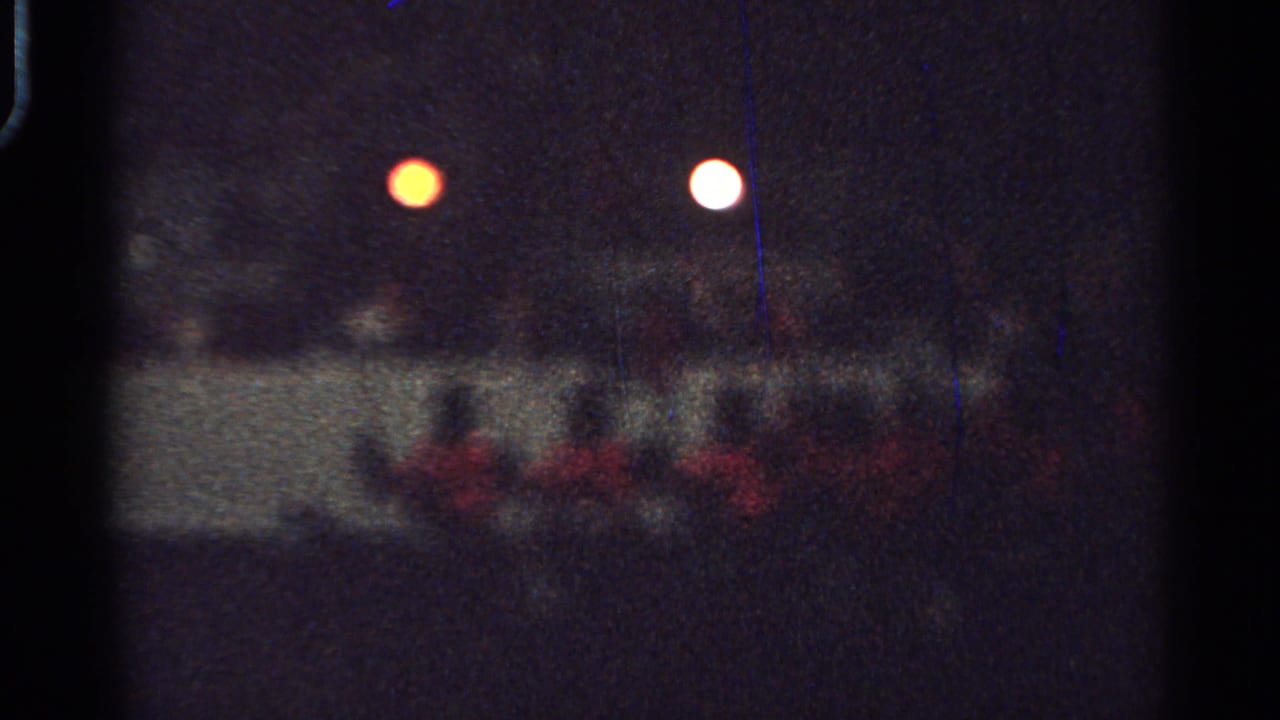 Distant 1965 Saint Louis home-movie frame of red-coated riders on horseback moving together at night.