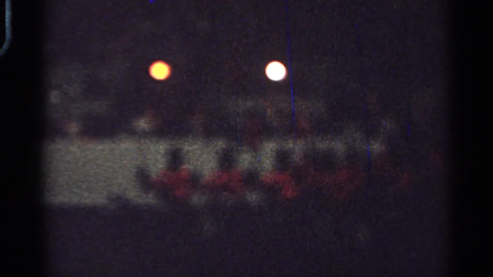 Distant 1965 Saint Louis home-movie frame of red-coated riders on horseback moving together at night.