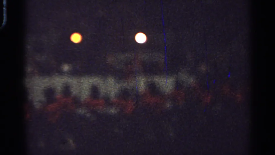 Grainy 1965 Saint Louis frame with a blurred group moving through darkness under two bright circular lights.
