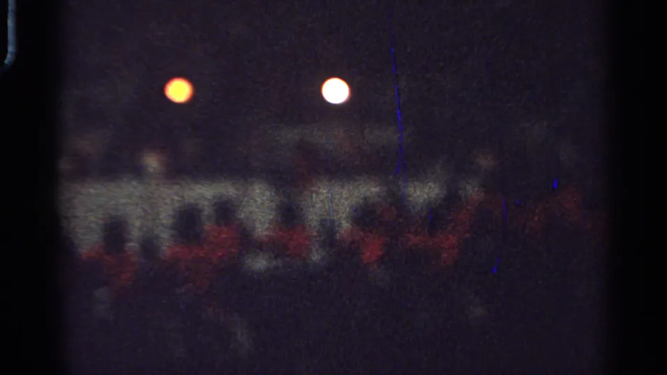 Low-exposure Saint Louis 1965 frame with red-shirted people or riders clustered under bright night lights.