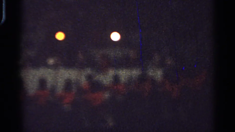 1965 Saint Louis night footage frame showing faint red-clad figures below orange and white lights, with visible film wear.
