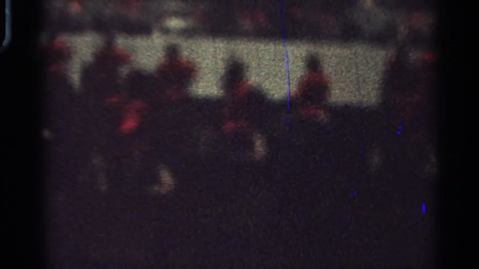 Grainy 1965 home-movie frame with mounted parade participants in red coats and dark horses at night.