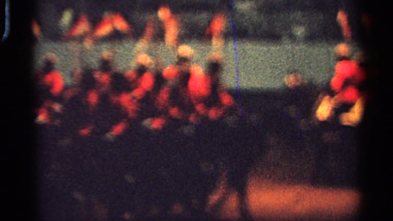 1965 Saint Louis parade frame with red-jacketed riders on horses moving beside a crowd behind a pale barrier.