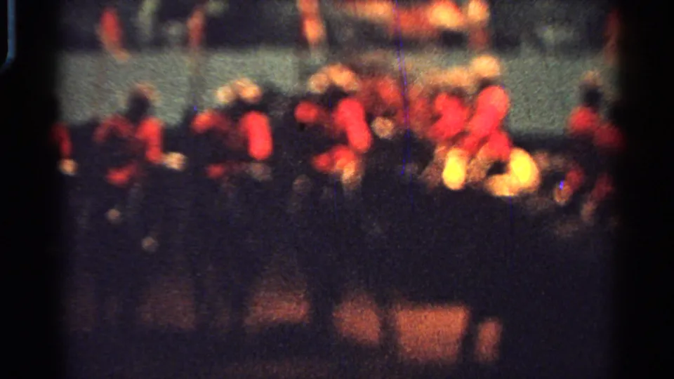 1965 Saint Louis home-movie frame showing horseback riders in red jackets and light hats crossing the parade area.