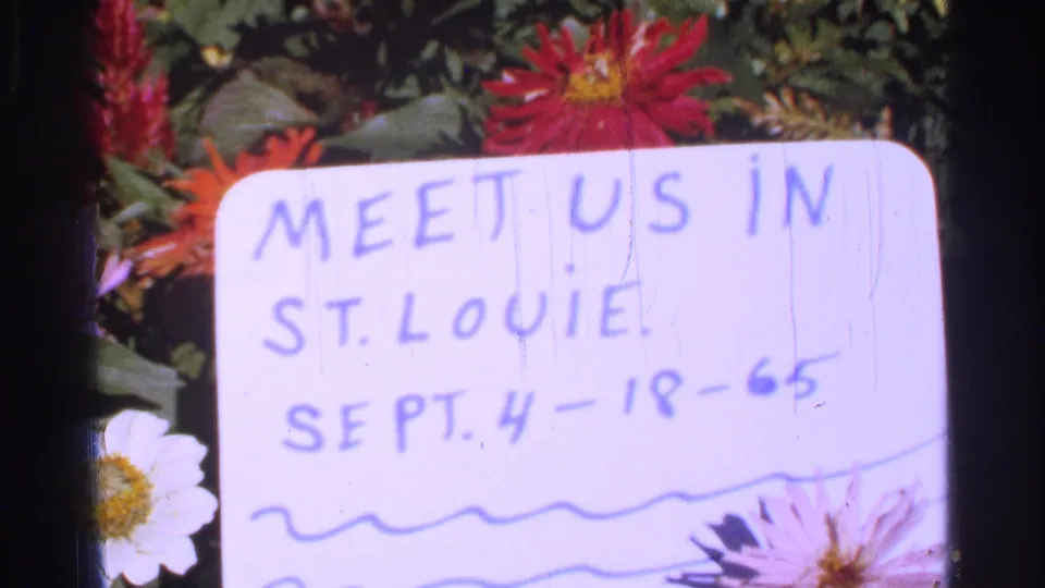 Pink-shifted 1965 8mm frame showing the St. Louie handwritten note, date, flowers, and visible film wear.