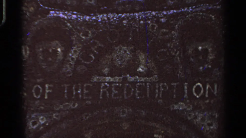 Close 8mm view of weathered stone lettering reading part of Grotto of the Redemption, with heavy grain and low light.