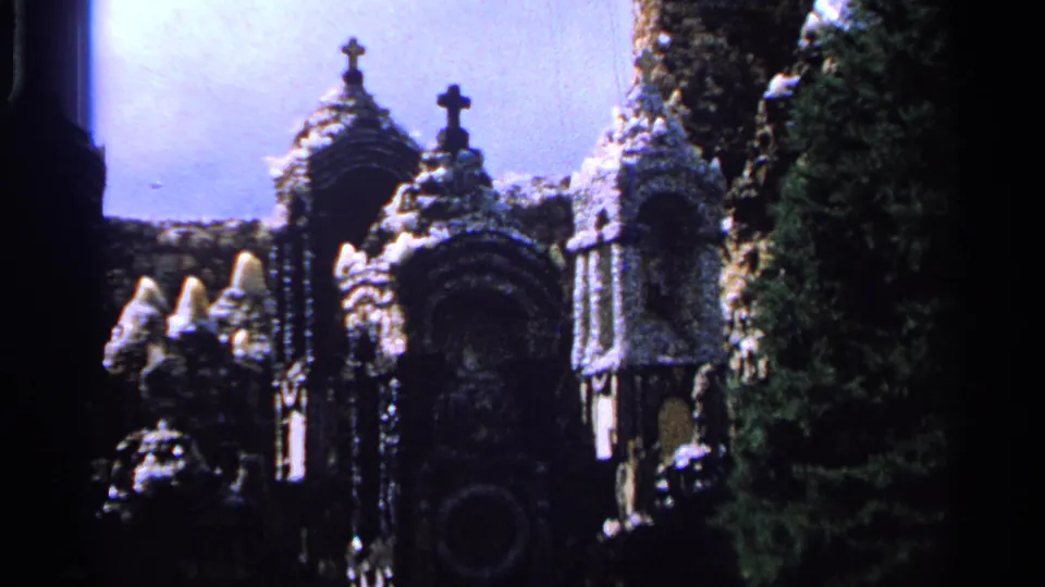 1965 Saint Louis frame showing clustered stone garden architecture with cross finials, arched details, and surrounding trees.