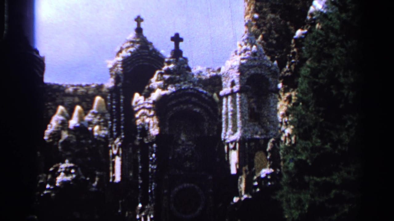 Stone religious shrine with arched niches, crosses, carvings, and dark trees under a pale sky.