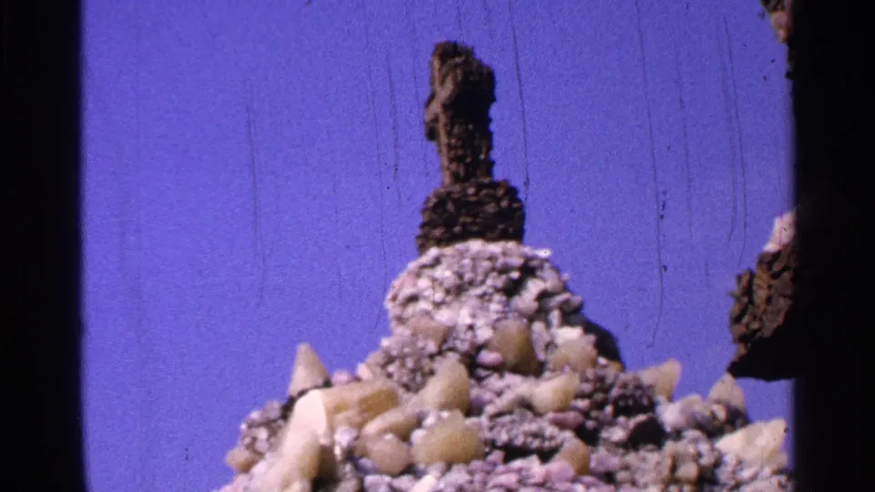 Closer 1965 Saint Louis frame showing a textured stone shrine detail with a religious figure or bust silhouetted against blue sky.