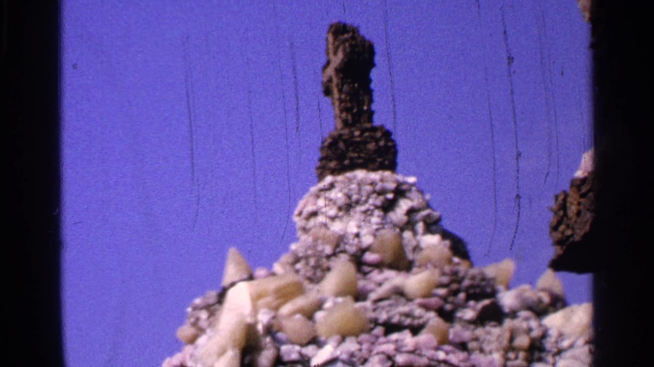 Rocky religious display with a dark cross form and blue backdrop.