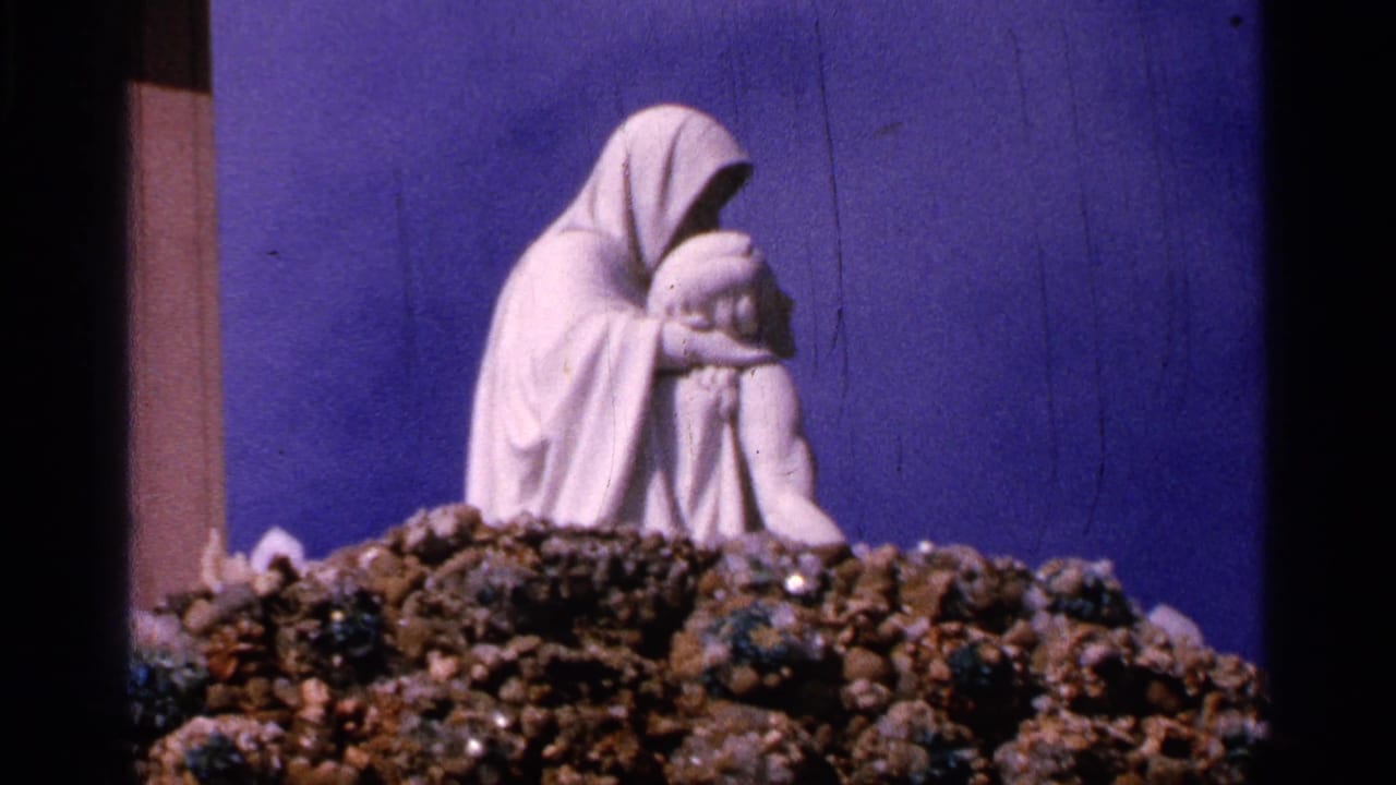 1965 Saint Louis frame with a white Pieta-like sculpture set on rocks, partially divided by dark film or display framing.