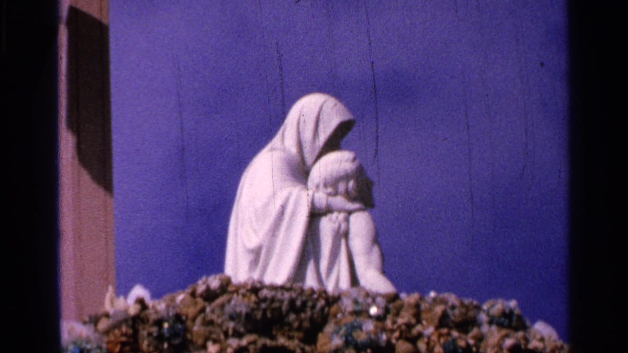 1965 Saint Louis home-movie view of a Pieta-like white sculpture centered over a rocky display with visible film scratches.