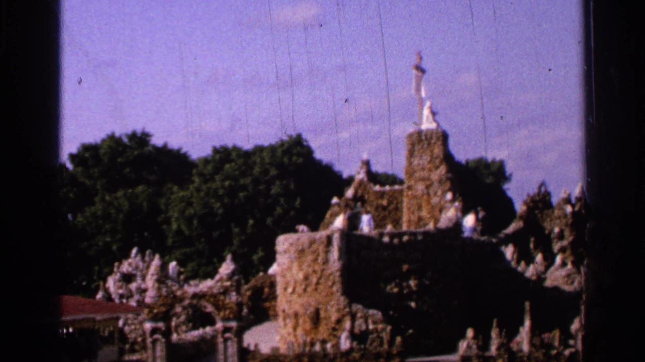 Stone religious display with statues, trees, sky, and dark 8mm frame borders.