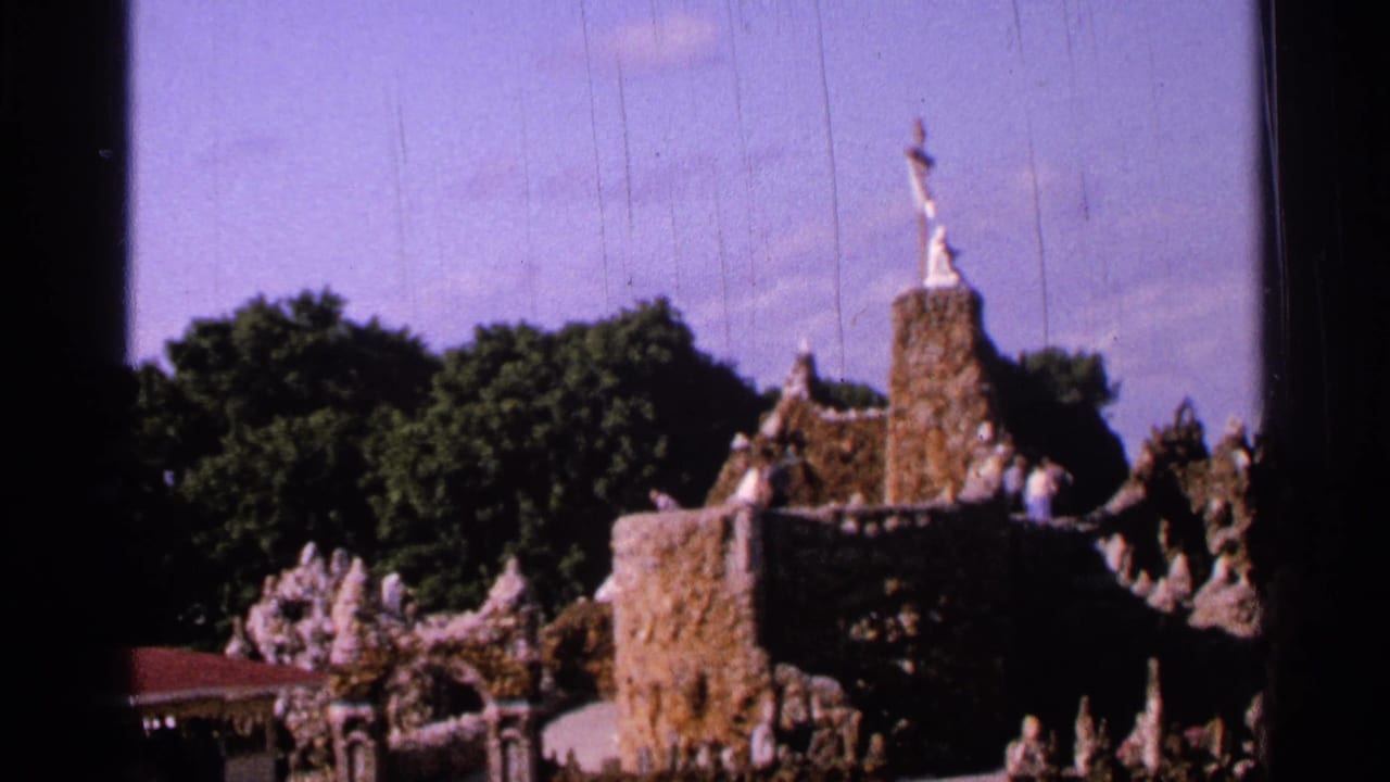 1965 Saint Louis frame of a stone religious display with a cross-topped tower, sculptural figures, trees, and purple-blue sky.