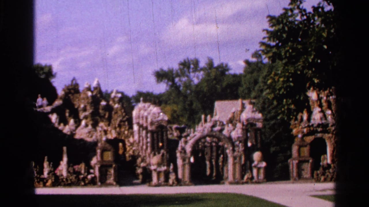 1965 Saint Louis 8mm frame showing castle-like stone garden forms, arched openings, trees, lawn, and a curved paved path.