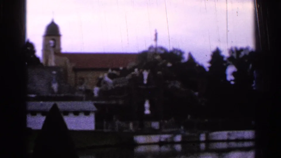 1965 Saint Louis 8mm frame showing a church steeple and roofline beyond trees, with dark foreground shapes and soft focus.