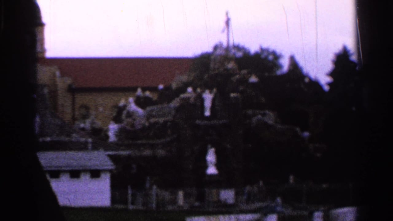 Distant church and religious grotto with white statues across water.