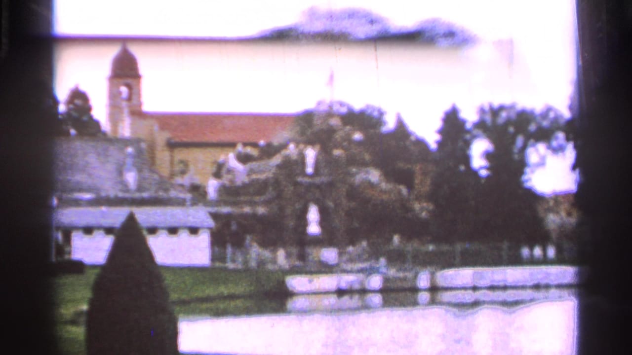 Saint Louis, Missouri 1965 frame with a bell-tower church behind a landscaped grotto, lawn, and low wall.