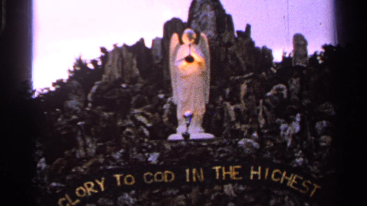 White angel sculpture holding a glowing light before a dark rocky backdrop.