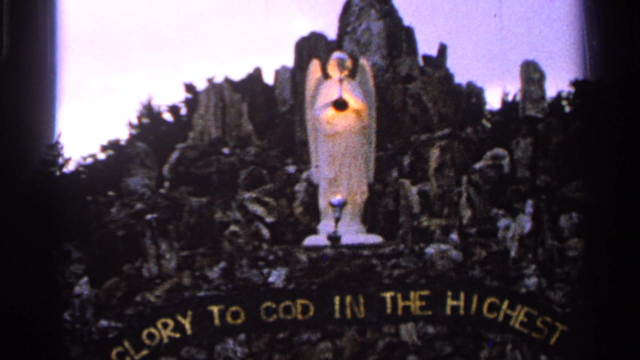 1965 Saint Louis home-movie frame of an illuminated angel figure above partial gold text reading Glory to God in the Highest.
